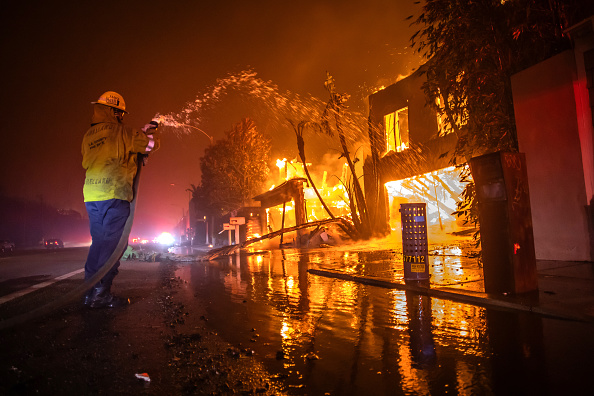 A firefighter battles the Palisades Fire while it burns homes at Pacific Coast Highway amid a powerful windstorm on January 8, 2025 in Los Angeles, California