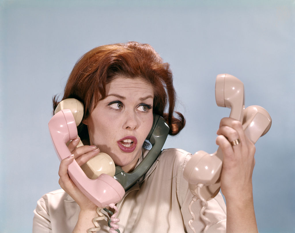 1960s FRUSTRATED YOUNG REDHEADED WOMAN TRYING TO ANSWER HANDLE FIVE TELEPHONE RECEIVERS