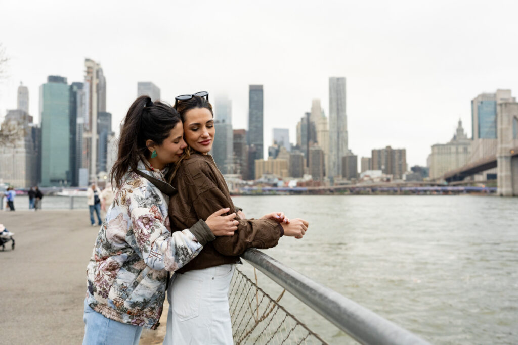 Lesbian couple embracing by the Hudson River in Brooklyn area, enjoying the moment together. Photo by Michele Pevide/Getty