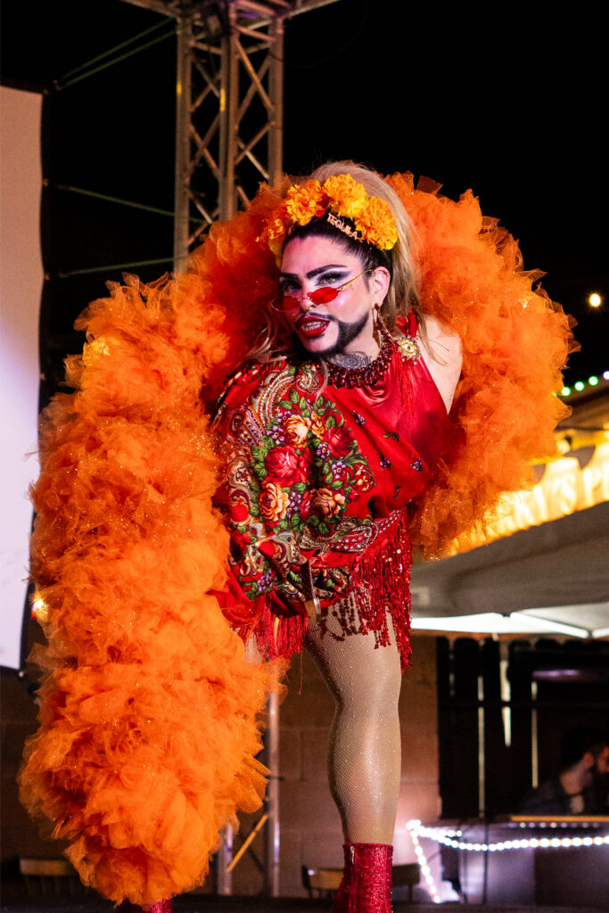 Papi Culo performs in an orange boa on stage. Photo by Fifth Eye Media