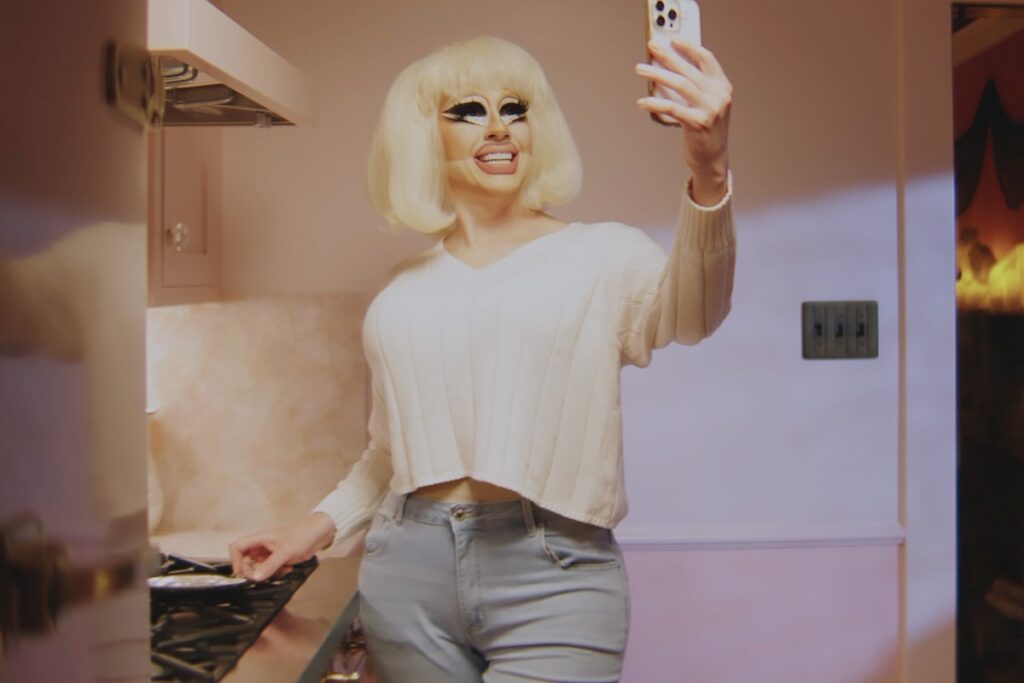 trixie in half drag holds up a cell phone